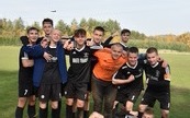 na zdjęciu grupa 10 os&oacute;b, wszyscy ubrani w czarne stroje sportowe, jeden chłopiec w pomarańczowej koszulce