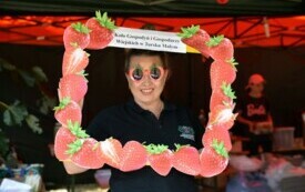 Kobieta nosi okulary w kształcie truskawek i trzyma tekturową ramkę z truskawek