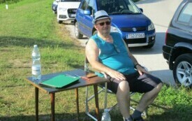 Mężczyzna siedzi na krześle przy stoliku, obok stoją samochody