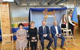 zdjęcie przedstawia 4 osoby, na uroczystości ślubowania pierwszych klas, po prawej stronie siedzi radny Rady Miejskiej Andrzej Baran, obok niego burmistrz Miasta i Gminy Jacek Nowak, obok niego sekretarz gminy Bogumiła Niespodziewana, oraz po lewej stroni