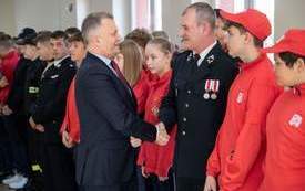 burmistrz Jacek Nowak wita się z przybyłym gościem, wśr&oacute;d nich grupa młodzieży