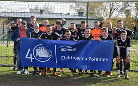 15 zawodnik&oacute;w wraz z trenerem dw&oacute;ch zawodnik&oacute;w w pomarańczowych koszulkach reszta w czarnych strojach reprezentująca czarnych Połaniec, grupa młodzieży trzymająca baner w rękach Enea Elektrownia Połaniec