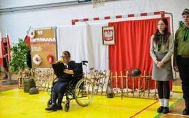 po prawej harcerze chłopiec i dziewczyna, a po lewej dziewczyna śpiewająca na w&oacute;zku inwalidzkim