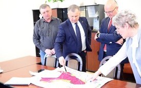 na zdjęciu 4 osoby, burmistrz wskazuje na mapie tereny pod inwestycję