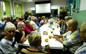 na zdjęciu seniorzy rozmawiają siedząc przy stołach