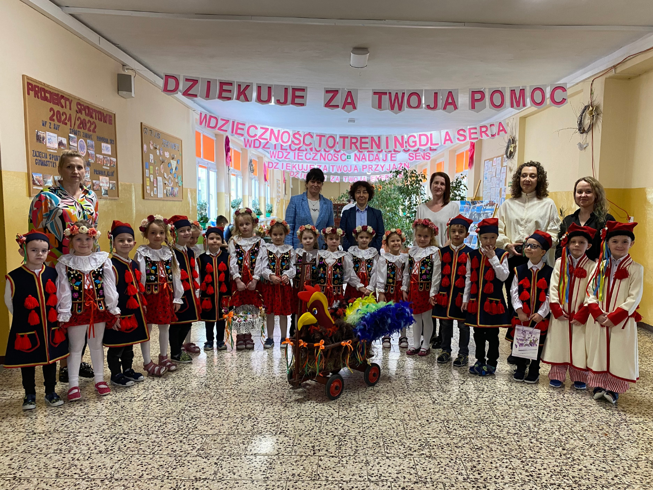 Na zdjęciu widoczna grupa przedszkolaków ubrana w stroje krakowiaków. Na zdjęciu również widoczni nauczyciele, opiekunowie i dyrektorzy przedszkola i szkoły.